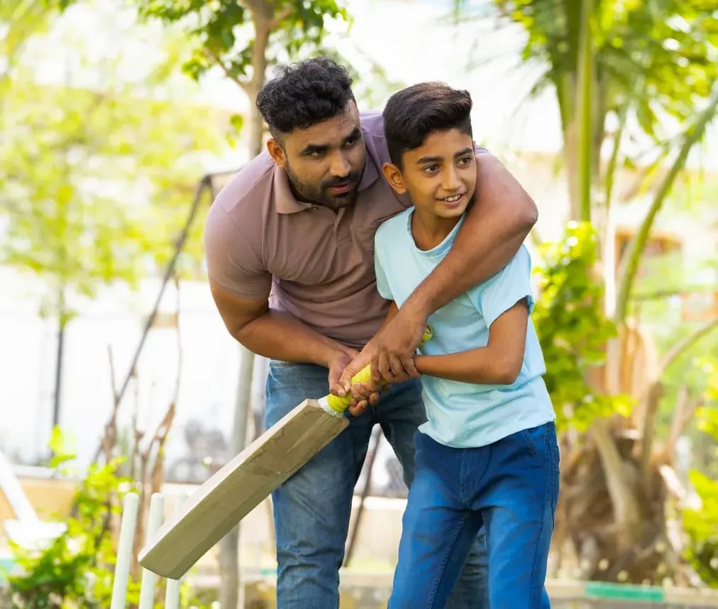 A father and son playing cricket together in a park