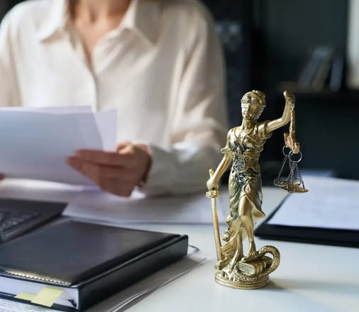 A statue of Lady Justice on a desk while a lawyer reviews documents in the background