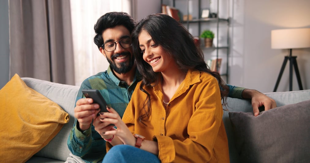 Smiling couple sitting on their sofa looking at a phone together