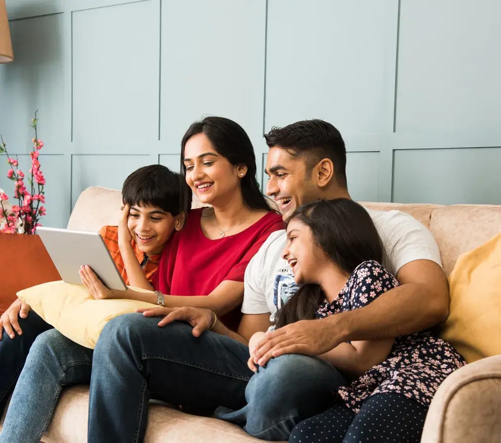 A family of four sitting together on a sofa, smiling at a tablet
