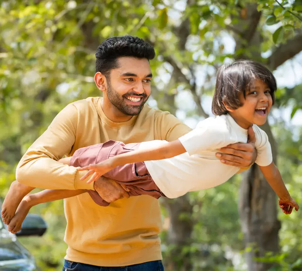 A father playfully swinging his laughing young son in the air outdoors